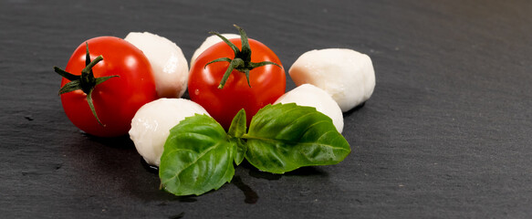 Mozzarella cheese, basil and tomato cherry on slate stone board, copy space