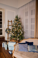 Stylish room with a large Christmas tree, decorated with a garland, golden balls,blue ornaments, flowers, pine cone. Fashionable sofa with pillows.Interior.Classical Christmas decor. New year.