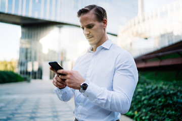 Handsome entrepreneur watching web video while messaging with partners using 4g internet connection on modern cellphone technology, good looking businessman making web booking and banking via mobile