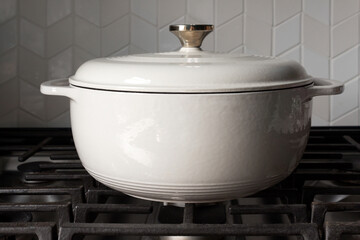 a large, white enameled cast iron crock pot on an unlit stove top with lid on in natural lighting against a chevron tile backsplash