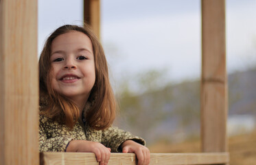 Beautiful little blonde girl  sits on a bench  smile at the camera in the park, Autumn season.