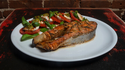 Caprese salad with cherry tomatoes, mozzarella toast and grilled salmon fish on the red brick wall background. Healthy eating concept.