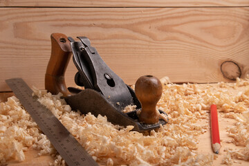 an old carpenter plane, a steel ruler and a pencil on a wooden background with shavings