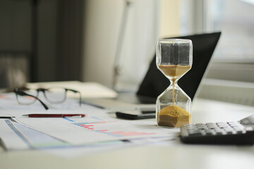 Hourglass and computer standing on graph or analytical papers, business  concepts.