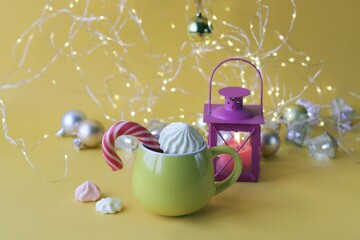 
Merry Christmas, yellow cup of coffee with meringues and caramel, lantern with a burning candle, Christmas decorations and illumination on a bright background