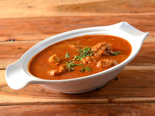 Kolhapuri Mutton masala or Kolhapuri Mutton tambda rassa or red meat curry is authentic indian spicy lamb gravy dish.Cooked with Indian spices,served over a rustic wooden background, selective focus