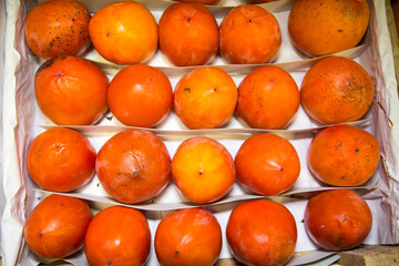 Sharon persimmon in a box stacked in rows of bright orange color. Fruits vegetables berries useful products agriculture.