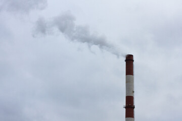 black acrid smoke from an industrial large chimney, close-up against the background of a cloudy sky. Environmental pollution