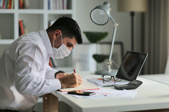 Young businessman wearing protective face mask while working on laptop at home office. During the quarantine.