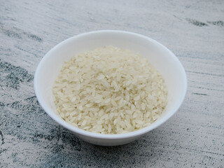 Grains of white yellow raw rice in a white bowl.