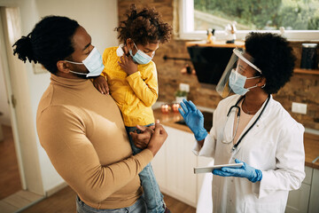 Black female doctor talking to father and daughter while visiting them at home during coronavirus pandemic.