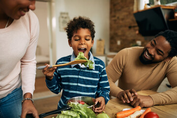 Cute African American boy eating salad in the kitchen.