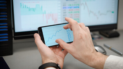 The trader works with electronic reports on the rates of crypto currencies. The bitcoin course is changing rapidly, and you can make good money on this. A man in a shirt in his workplace.
