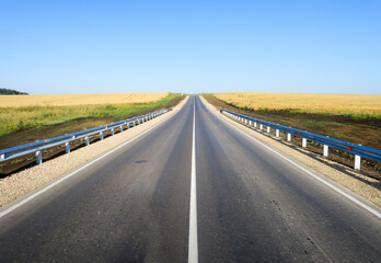 New asphalt road surface on the background of green and yellow fields to the horizon. The...