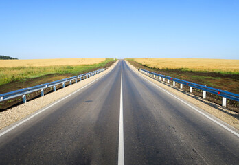 New asphalt road surface on the background of green and yellow fields to the horizon. The construction site for the road works. Highway on the background of a rural landscape        