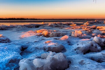 A view of a river covered in ice illuminated by the orange light of the sun at sunset. Winter landscape