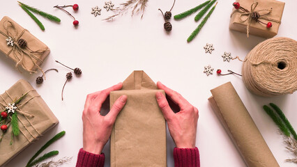 Step 5.Step by step instruction to eco friendly and zero waste Christmas gift wrapping.Woman wraps gift in brown paper and seals edges with glue,top view,flat lay.