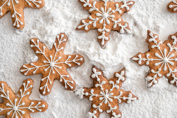 Home-baked gingerbread snowflakes decorated with sugar glaze. Top view, close-up on textured white powdered sugar background.