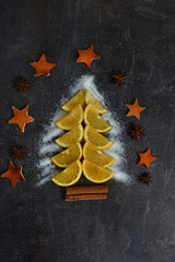 Creative Christmas tree made of orange slices and cardamon, cinnamon on a black background. Holiday-cards. Merry Christmas.