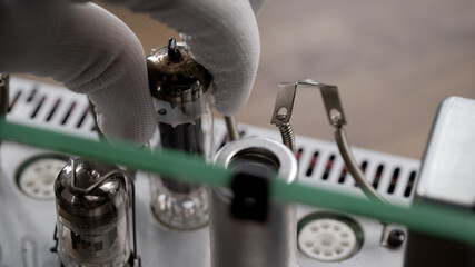 An engineer in a repair shop is replacing old radio tubes. The hand removes the vacuum tube from...