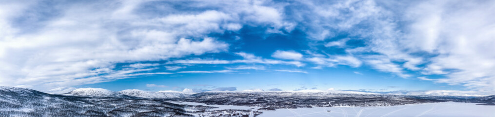 Scenic wide aerial panorama view on Scandinavian Mountains close to Joesjo lake in Swedish Lapland in winter cover, frosty day. Much snow, frozen lakes, birch trees with Mountain Tops at background