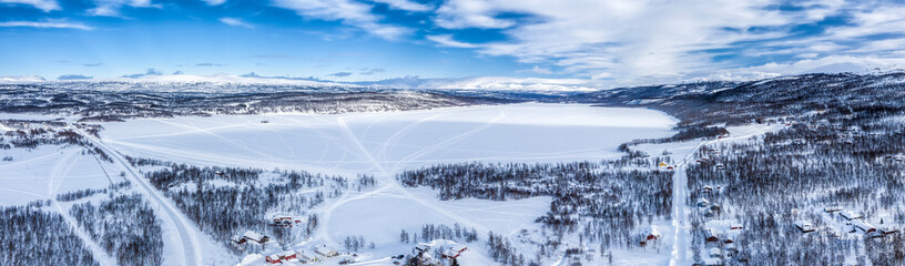 Scenic aerial view on Tarna Vilt village and Joesjo lake in Swedish Lapland in winter cover, frosty sunny day. Roads, houses, frozen lakes, birch trees with Scandinavian mountains at background