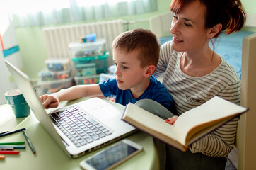 Mother using laptop teaching with her son online at home in his room.
