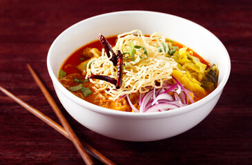 Bowl of Thai Khao Soi in a white bowl on a dark table with chopsticks; copy space