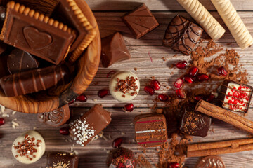 A bowl of assorted chocolates and chocolate biscuits on wooden background with cacao powder cinnamon sticks, pirouettes and coconut sprinkles creating an organic look. For Valentines day and christmas © Grandbrothers