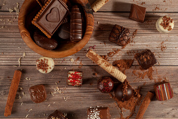A bowl of assorted chocolates and chocolate biscuits on wooden background with cacao powder cinnamon sticks, pirouettes and coconut sprinkles creating an organic look. For Valentines day and christmas © Grandbrothers