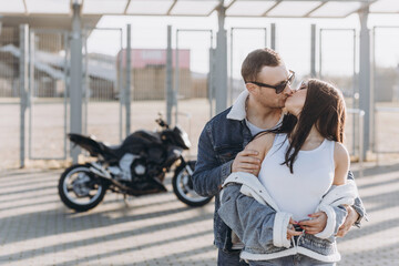 Fototapeta na wymiar Sexy girl and guy hugging and kissing on the background of a sports motorcycle standing in the parking lot near a large football stadium