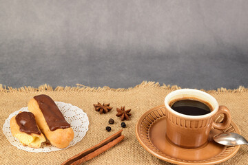 Side view of cut eclair and a hot cup of coffee lying on a linen napkin