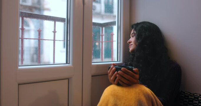 Latina woman sitting looking out the window drinking coffee