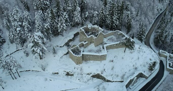 Aerial drone overhead view of medieval Predil fortress in Slovenia. Paved countryside road between forest. Cold winter in Alpine valley. Beautiful landscape covered with snow
