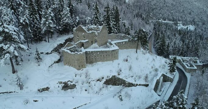 Aerial drone view of medieval Predil fortress in Slovenia. Paved countryside road between forest. Cold winter in Alpine valley. Beautiful landscape covered with snow. Parallax moving
