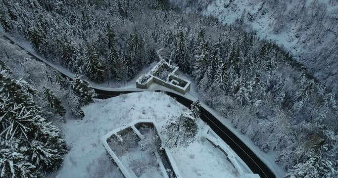 Aerial drone overhead view of medieval Predil fortress in Slovenia. Paved countryside road between forest. Cold winter season in Alpine valley. Beautiful landscape covered with snow. Forward moving