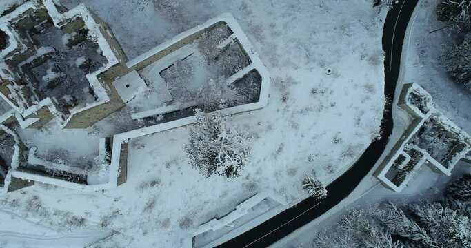Aerial drone overhead view of medieval Predil fortress in Slovenia. Paved countryside road between forest. Cold winter season in Alpine valley. Beautiful landscape covered with snow