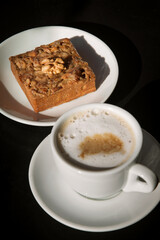walnut cake on a white plate next to a Cup of cappuccino, Sunny photo. 
