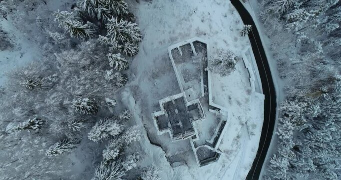 Aerial drone overhead view of medieval Predil fortress in Slovenia. Paved countryside road between forest. Cold winter season in Alpine valley. Beautiful landscape covered with snow. Forward moving