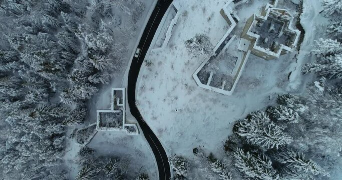 Aerial drone overhead view of medieval Predil fortress in Slovenia. Paved countryside road between forest. Cold winter season in Alpine valley. Beautiful landscape covered with snow. Forward moving