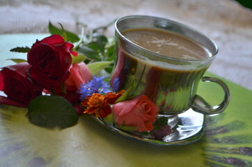 kawa w srebrnej filiżance , czerwone róże i kolorowe kwiaty