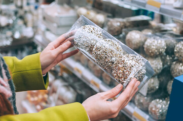 The girl holds decorative balls in her hands to decorate Christmas and New Year. Against the background of the supermarket counter.