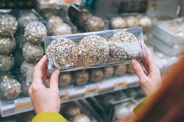 Close-up, a girl holds decorative balls in her hands to decorate Christmas and New Year. Against the background of the supermarket counter.