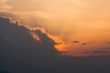 Ciemnopomarańczowe niebo. Zachodzące słońce schowane za ciemną chmurą. Promienie słońca.