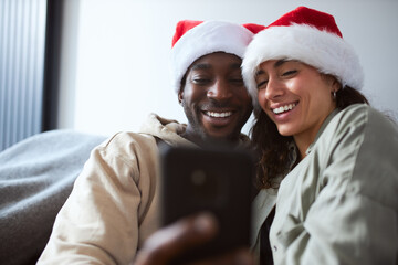 Young Smiling Couple Wearing Santa Hats At Home Posing For Christmas Selfie On Mobile Phone Together