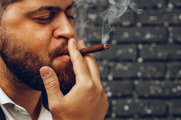 Bearded man smoking cigar against black brick wall