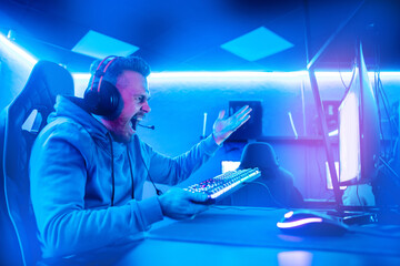 Streamer young man angry screams defeat professional gamer playing online games computer with headphones, neon color © Parilov