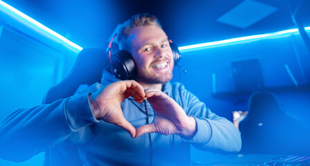 Streamer beautiful man shows heart sign with hands professional gamer playing online games computer, neon color © Parilov