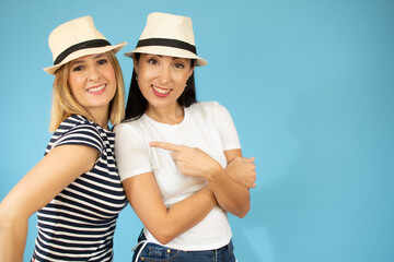 Two cheerful pretty young girls smiling with hat isolated over blue background