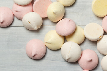 Pastel-colored meringues on a light wooden surface, close-up, top view with space